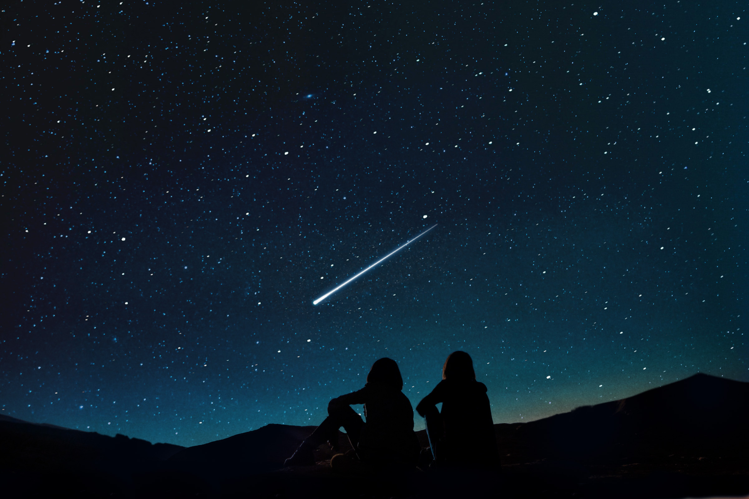 Two people sitting on at a high place looking at a starry sky with a bright shooting star streaking across it.